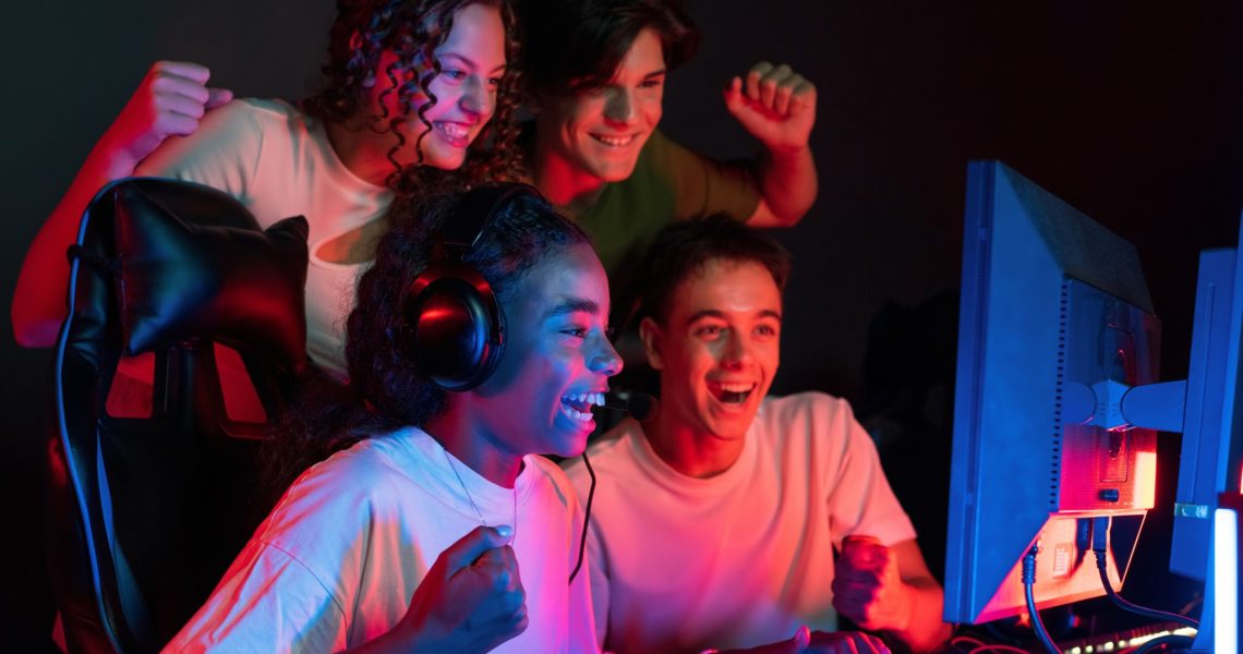 Group of multiracial teens playing video games in video game club with blue and red illumination. Excited because of a victory