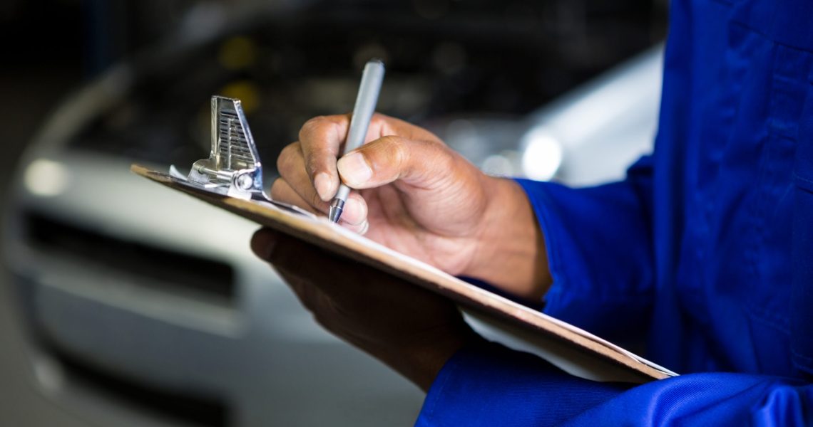 Mid section of mechanic preparing a check list at repair garage