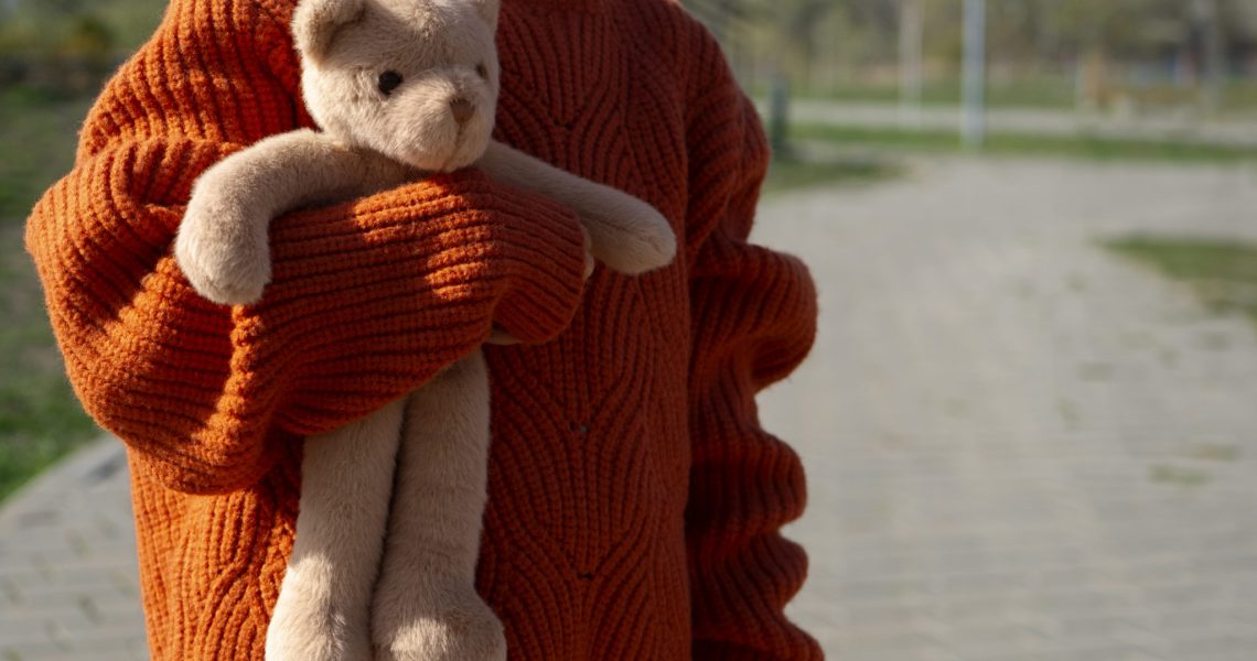 vista-frontal-de-uma-crianca-segurando-um-ursinho-de-pelucia-ao-ar-livre